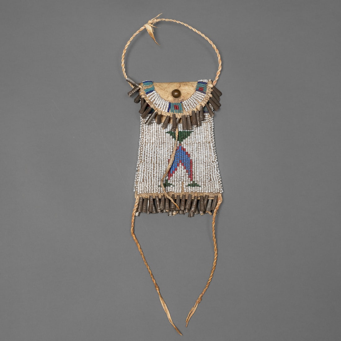 A Plains beaded hide Strike-a-light bag: Arapaho, fourth quarter 19th century, the pouch made from parfleche the front decorated in multicolored geometric design on white bead ground, the flap bead decorated with tin cone fringe, tin cones