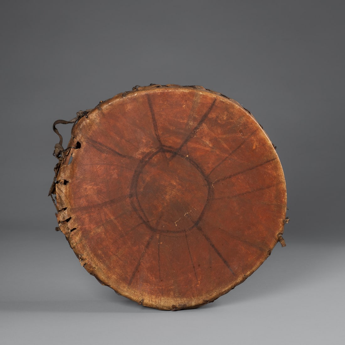 A Plains painted hide drum: Plains, fourth quarter 19th century, the stretched hide attached with leather strapping to the round wood form, with painted decoration on each side. Dia. 13 in.