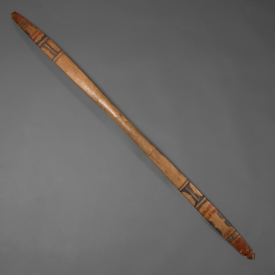 A Northwest Coast polychrome wood bow: Haida, 19th century, carved from a single piece of hardwood and decorated with red ochre painted bands forming wave and diamond motifs along both limbs. The surface shows smooth patination from