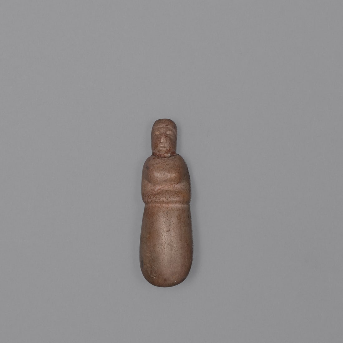 A carved Stone female effigy figure: Attributed to Western Great Lakes Region, a diminutive carved stone figure with a simplified, elongated body tapering to a rounded base, surmounted by a distinctly carved head with defined facial
