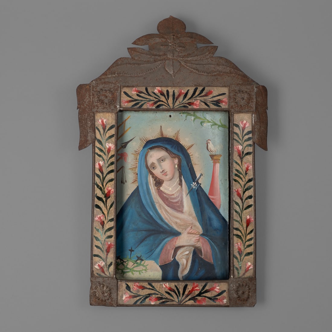 A New Mexican tin frame: The New Mexican painted tin frame, with circular repousse on the corners and top detailing, the sides are painted with pink and white floral elements, Mary is represented with blue, white, and pink