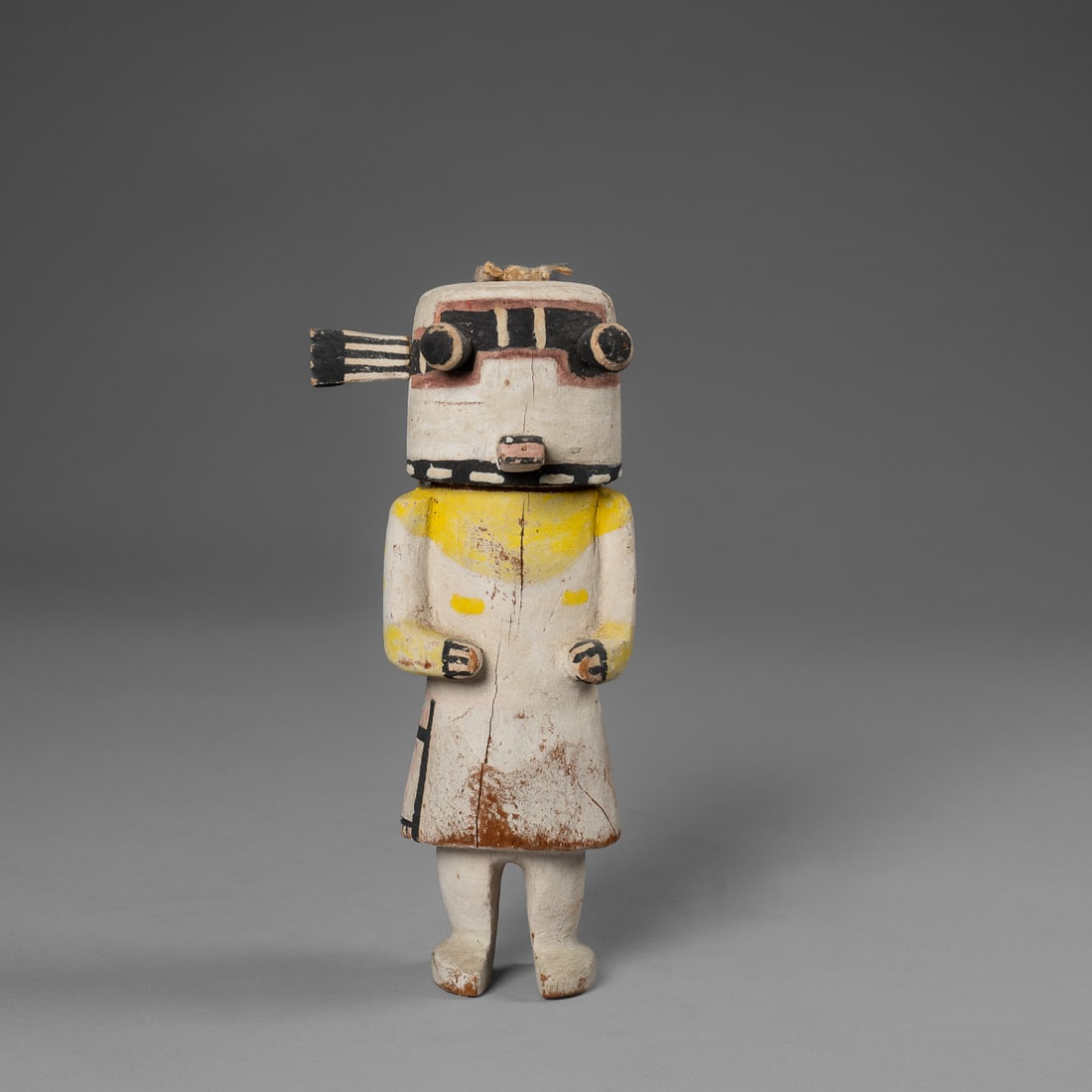 A Hopi kachina doll: Early 20th century, probably a Holi kachina, with bug eyes and square mouth, black band across the eyes, yellow painted shoulders and arms, with a simple sash. Ht. 8 in.