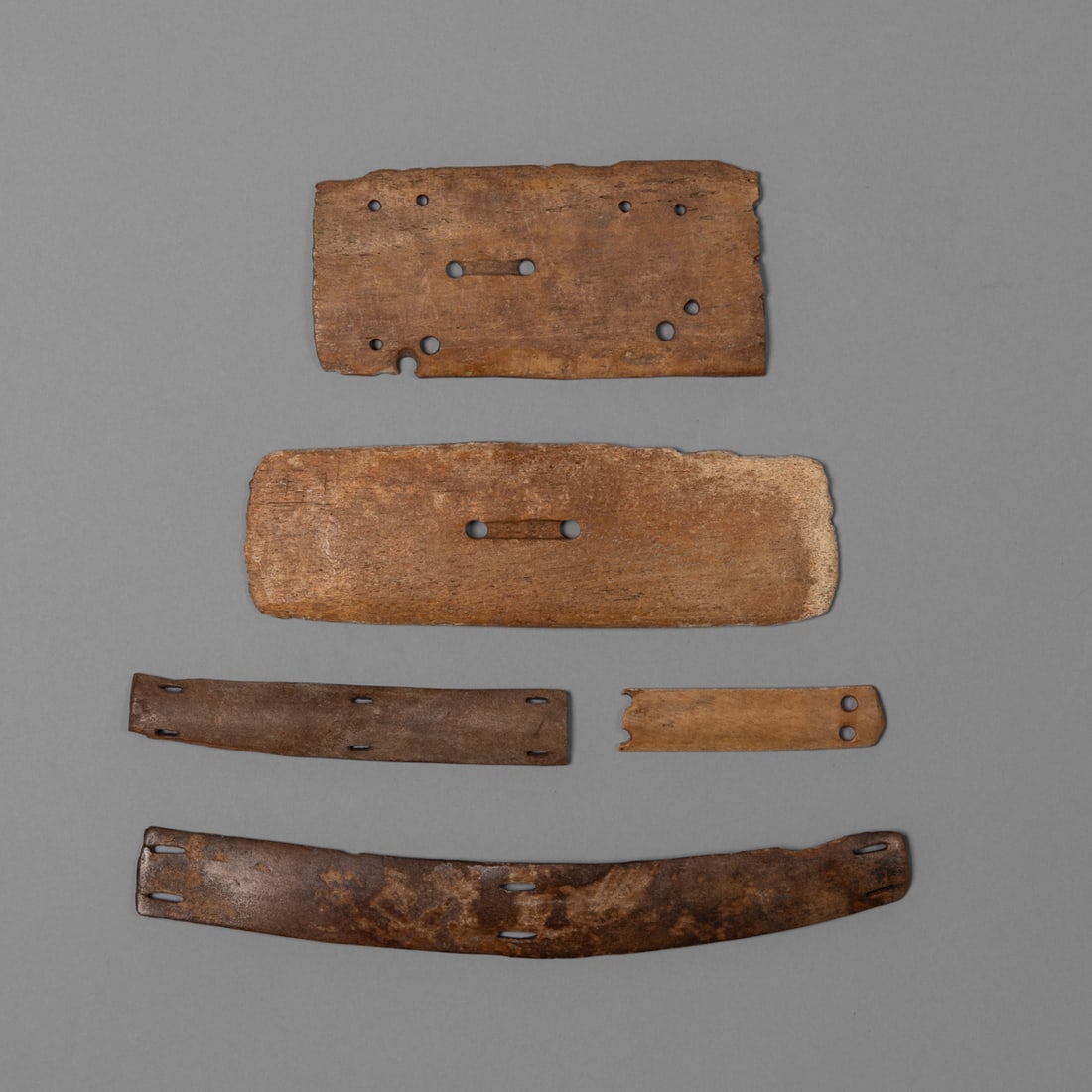 A collection of Northwest Coast armor: 19th century, or earlier, five pieces of bone armor each pierced for attachment to the chest armor garment, (some loss). Lg. 9 1/2, 7 1/8, 5 1/2, 5 3/8, and 3 1/4 in.