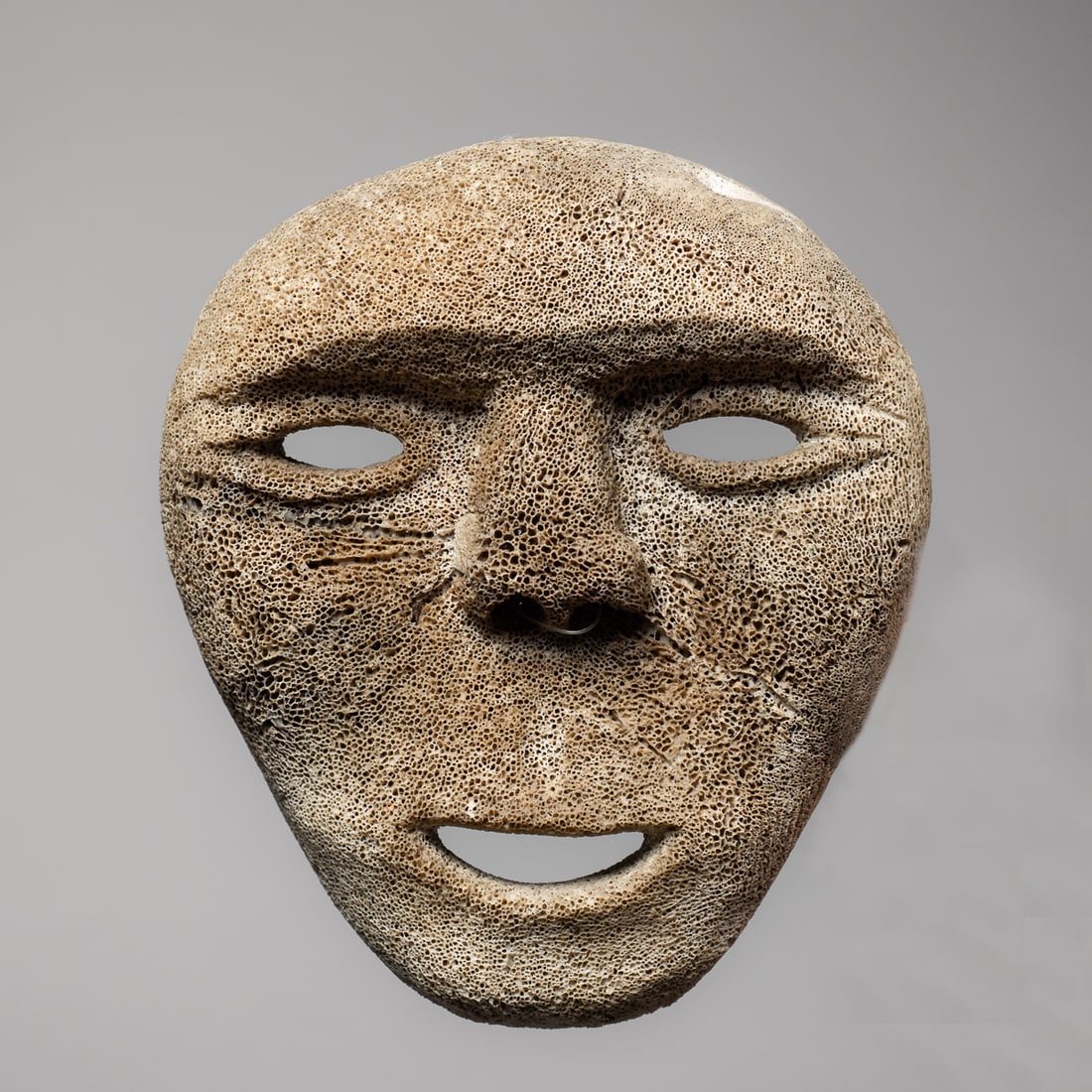 An Eskimo mask: Early 20th century, carved from bone, with cut-out mouth, eyes and nostrils. Size 6 1/2 x 5 3/4 in.
