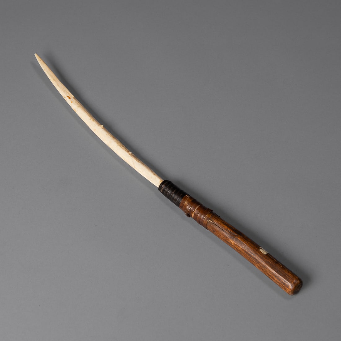 An Eskimo hunting dagger: Alaska, 19th century, the long slightly curving bone blade, with three small protrusions along one edge, attached to a wood handle with hide strapping, with old inventory number, "I-39." Lg. 16 1/2