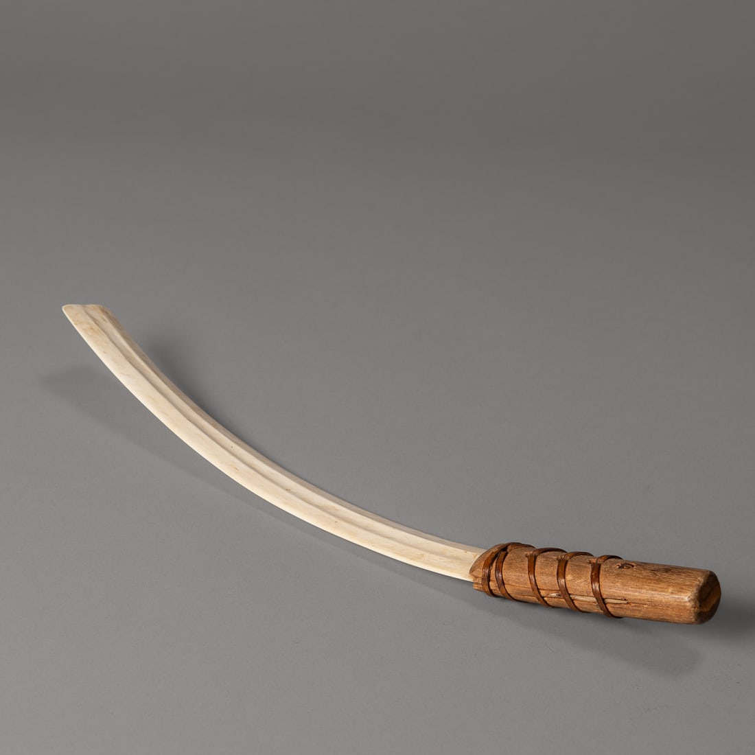 An Eskimo snow knife: Alaska, early 20th century, the curving, squared-off blade with medial groove on both sides, with wood handle attached with a stripped hide strapping, with "Nome Alaska, 1919," on one side. Lg. 13