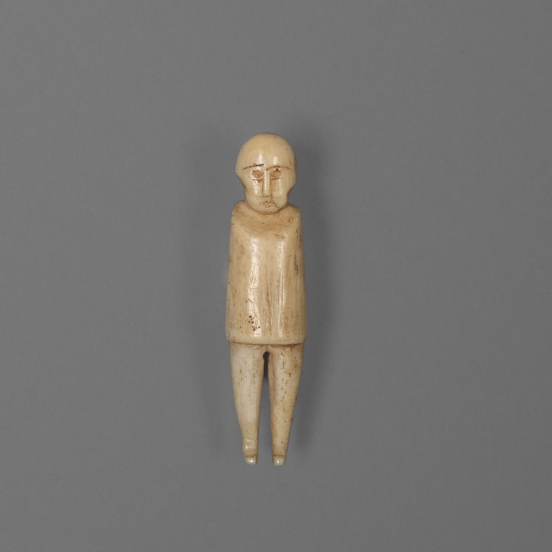 An Inupiaq carved bone shaman figure: Point Hope, Alaska, a small carved bone figure of a shaman, Inupiaq, from Point Hope, Alaska, nineteenth century, measuring two and one eighth inches long. The figure has a rounded head with simplifie
