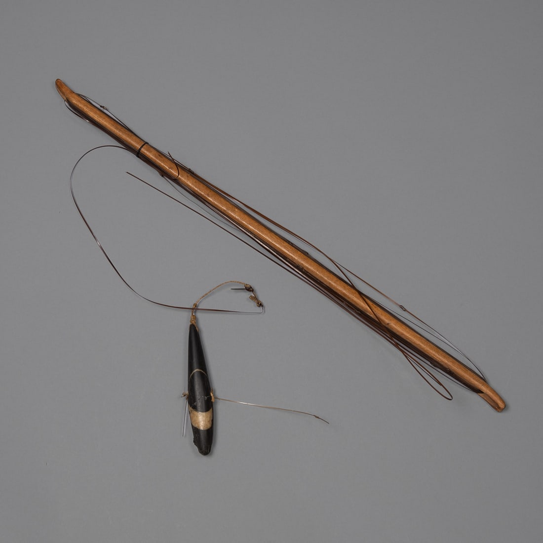 An Alaskan Eskimo Tom Cod and Sculpin Fishing Rod & weight: 19th century, A fine antique Native Alaskan fishing implement used for jigging Tom Cod and sculpin through sea ice, comprising a wooden winding staff of shuttle form, a baleen fishing line, and a