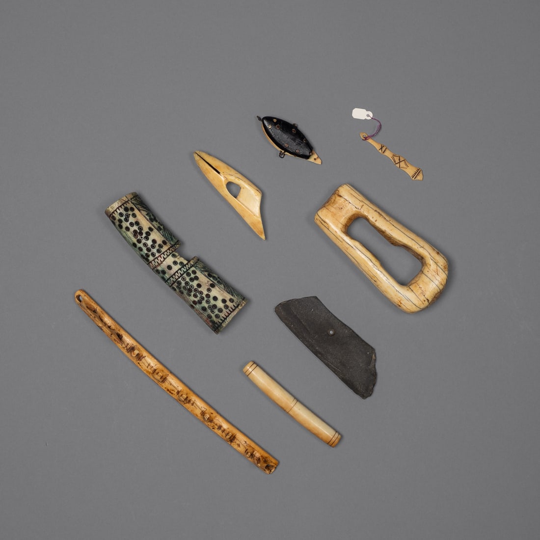 A collection of Eskimo artifacts: Alaska, 19th century and earlier, a bow drill fragment, a harpoon head, a needle case, a knife blade, part of a fish hook, a large container and small decorated item.
