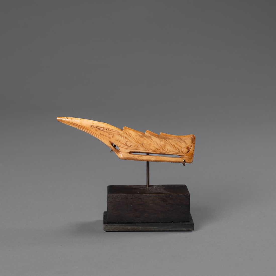 An Eskimo game hook: St Lawrence Island, Alaska, Punuk or Thule period, with fine incised decoration on both sides. Mounted on a custom base. Lg. 4 1/4, ht. 1 in.