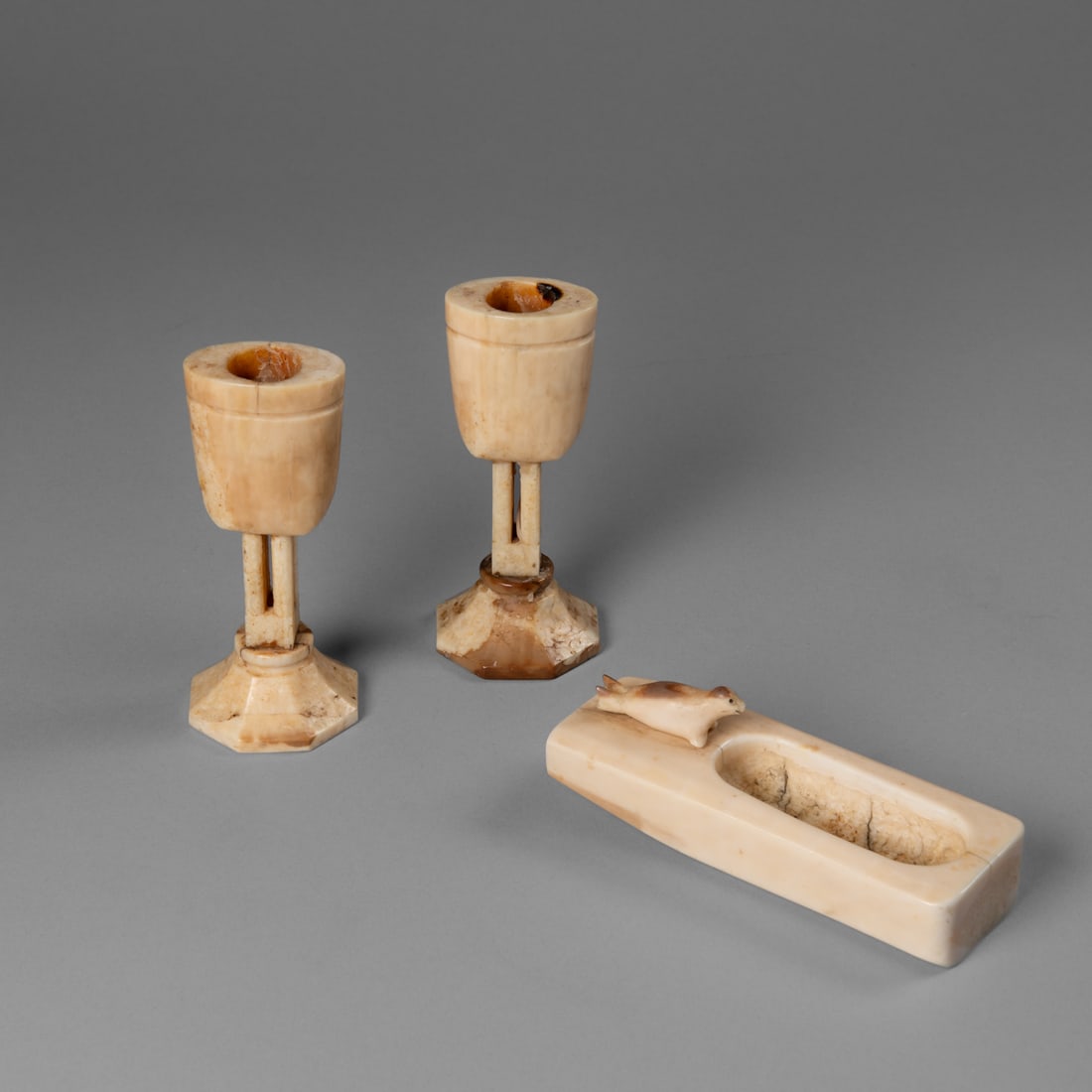 A pair of Eskimo candle sticks: Alaska, early 20th century, each carved with an octagon base below a four pillar collum mounting the candle holder, together with an ash tray, with carved seal on one side. (with wax residue). Ht. 5