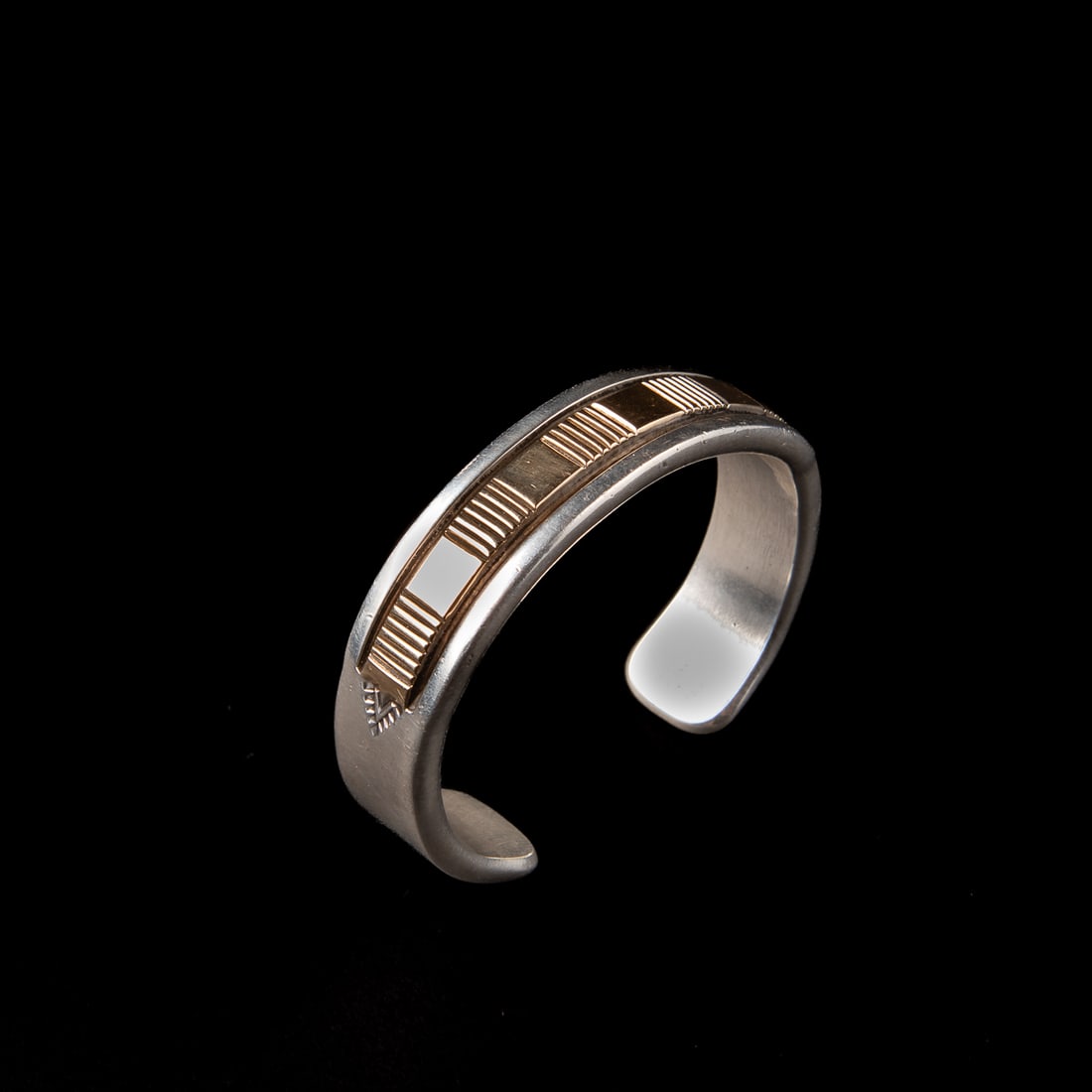 A Bruce Morgan silver and gold cuff bracelet: Bruce Morgan, Navajo (b. 1957), the heavy sterling cuff stamp decorated on the interior, the exterior with 14k gold channel with chisel and stamp work, marked with “B. Morgan. 14k Sterling.” T