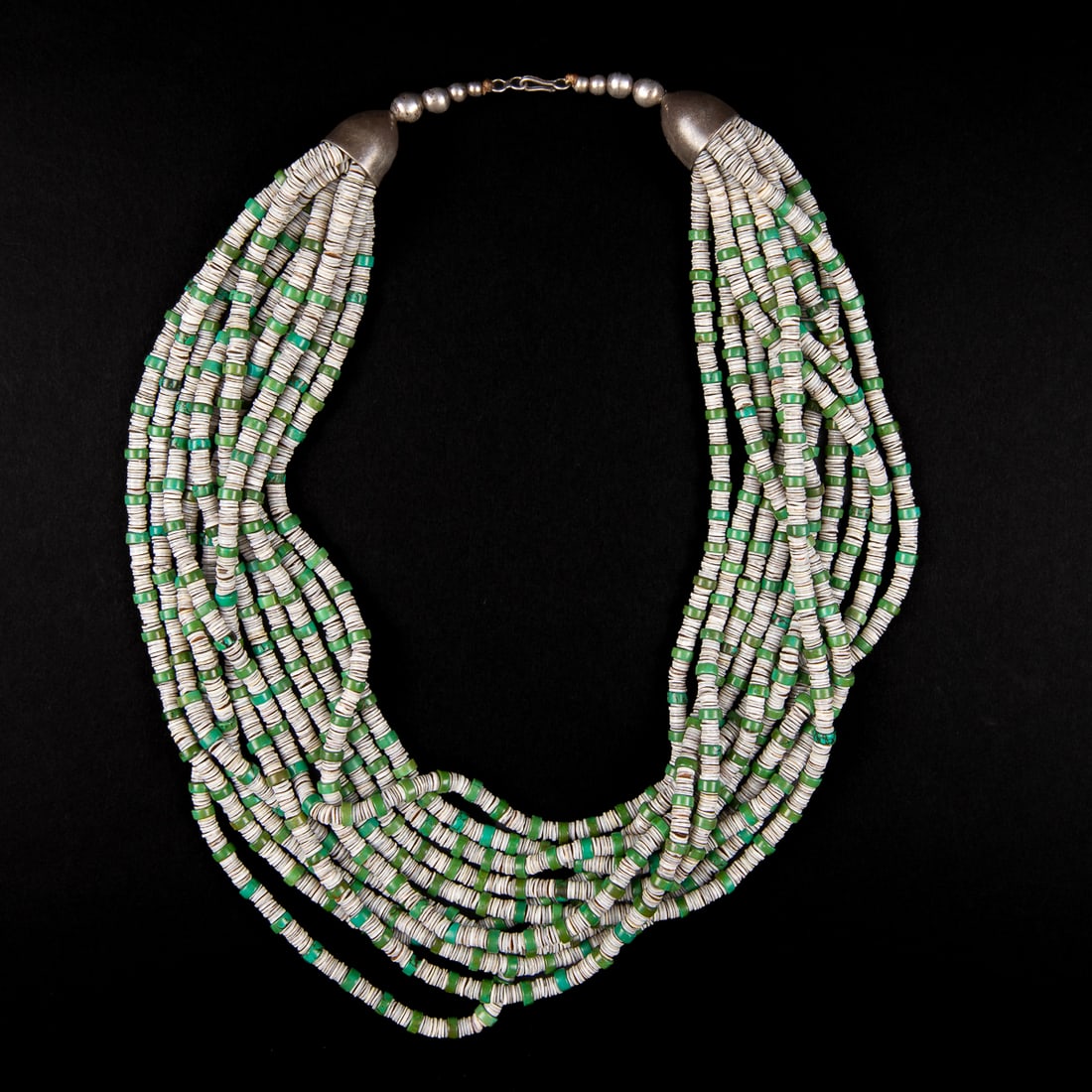A Southwest heishi necklace: The silver beaded clasp holds eleven strands of white, silver, and blue/green heishi evenly spaced apart that create uniform pattern. Lg. 12 in. clasped.