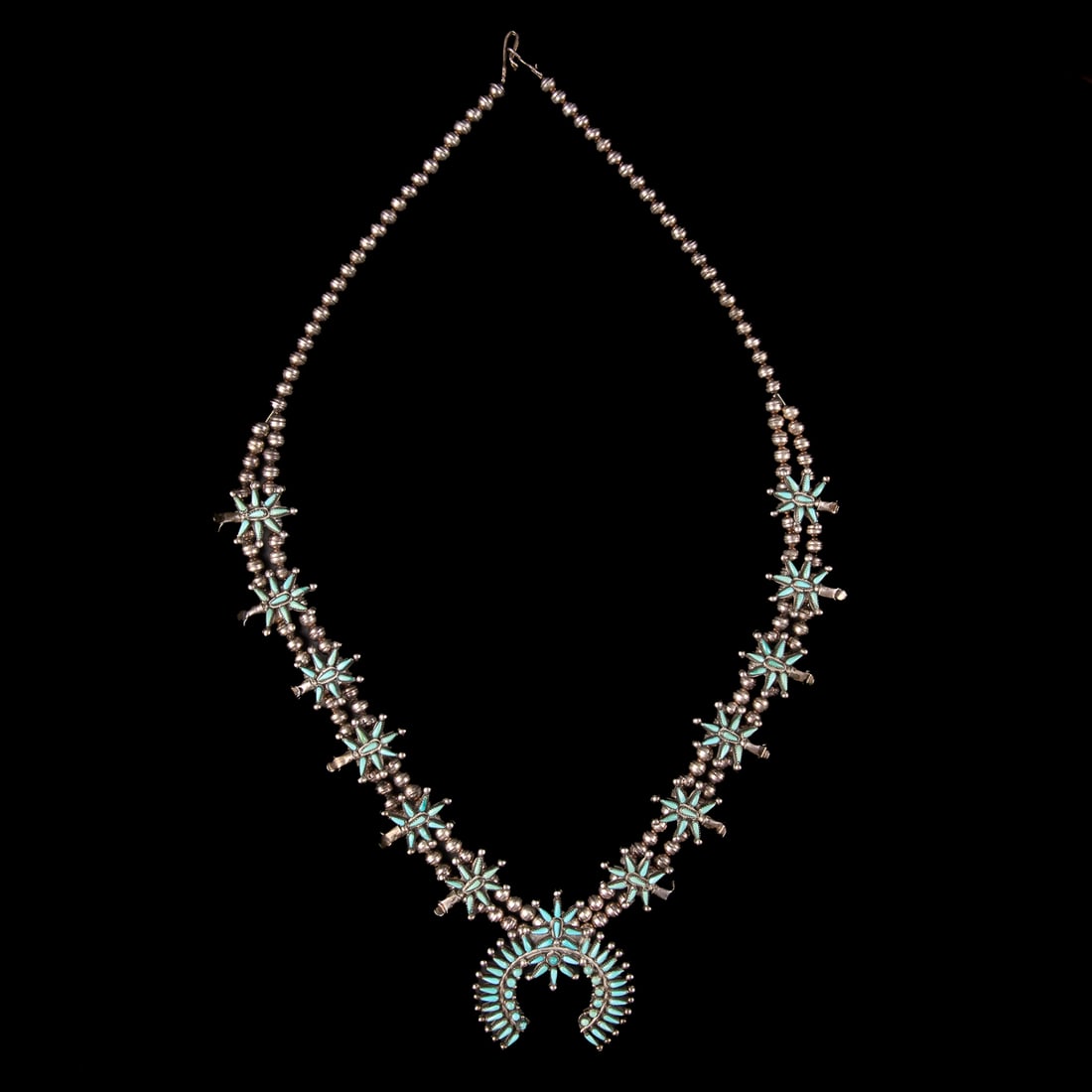 A Zuni petit-point silver and turquoise necklace: Designed as a single strand of silver beads branching to a double strand of silver beads strung with 12-star blossoms and a naja set with two star motifs and teardrop-shaped petit point turquoise
