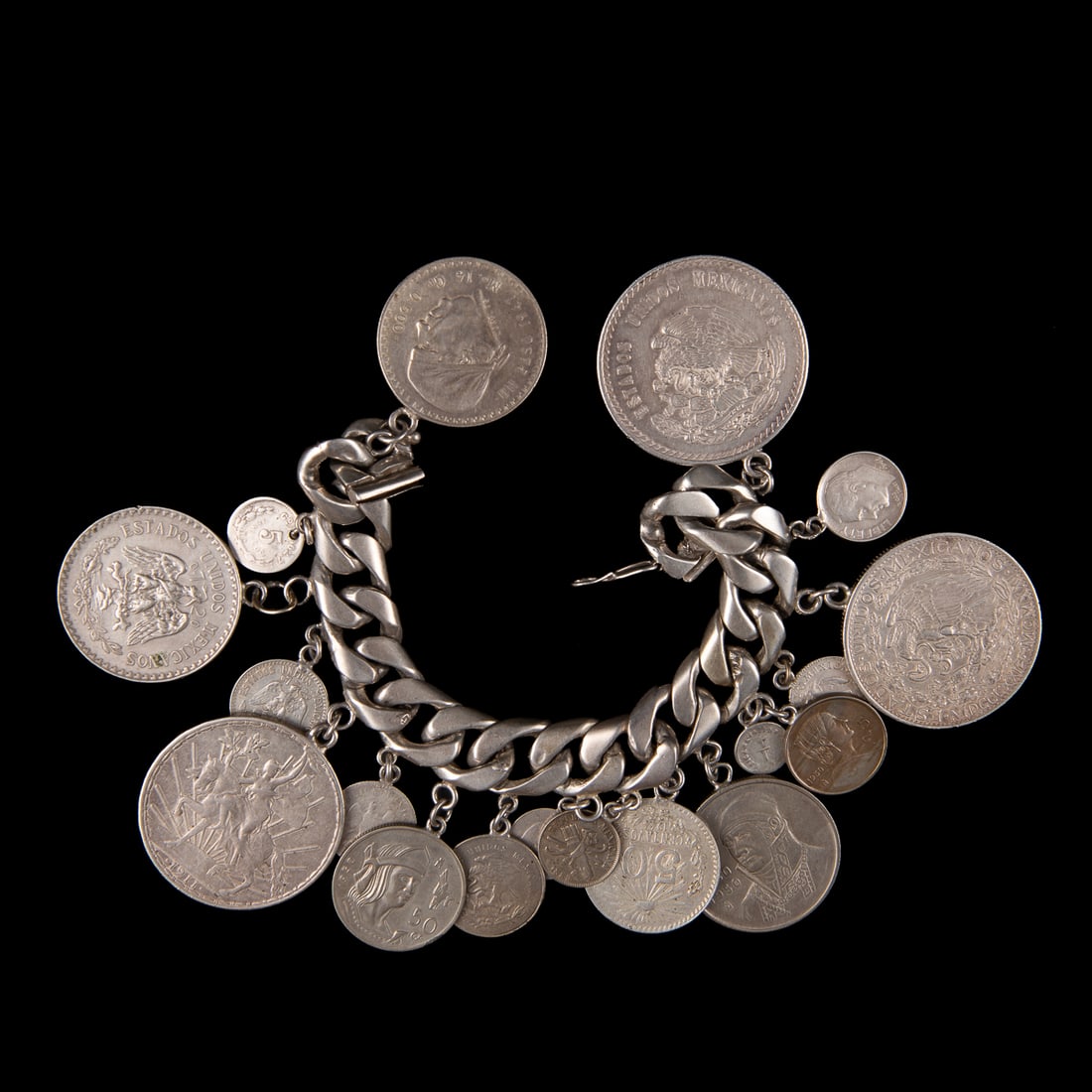 A Mexican silver coin bracelet: The thick silver chain with 18 peso-charms, each modeled after a different coin, marked “Mexico” on clasp. Lg. of chain 7 ¼ in, gross weight 257 grams.