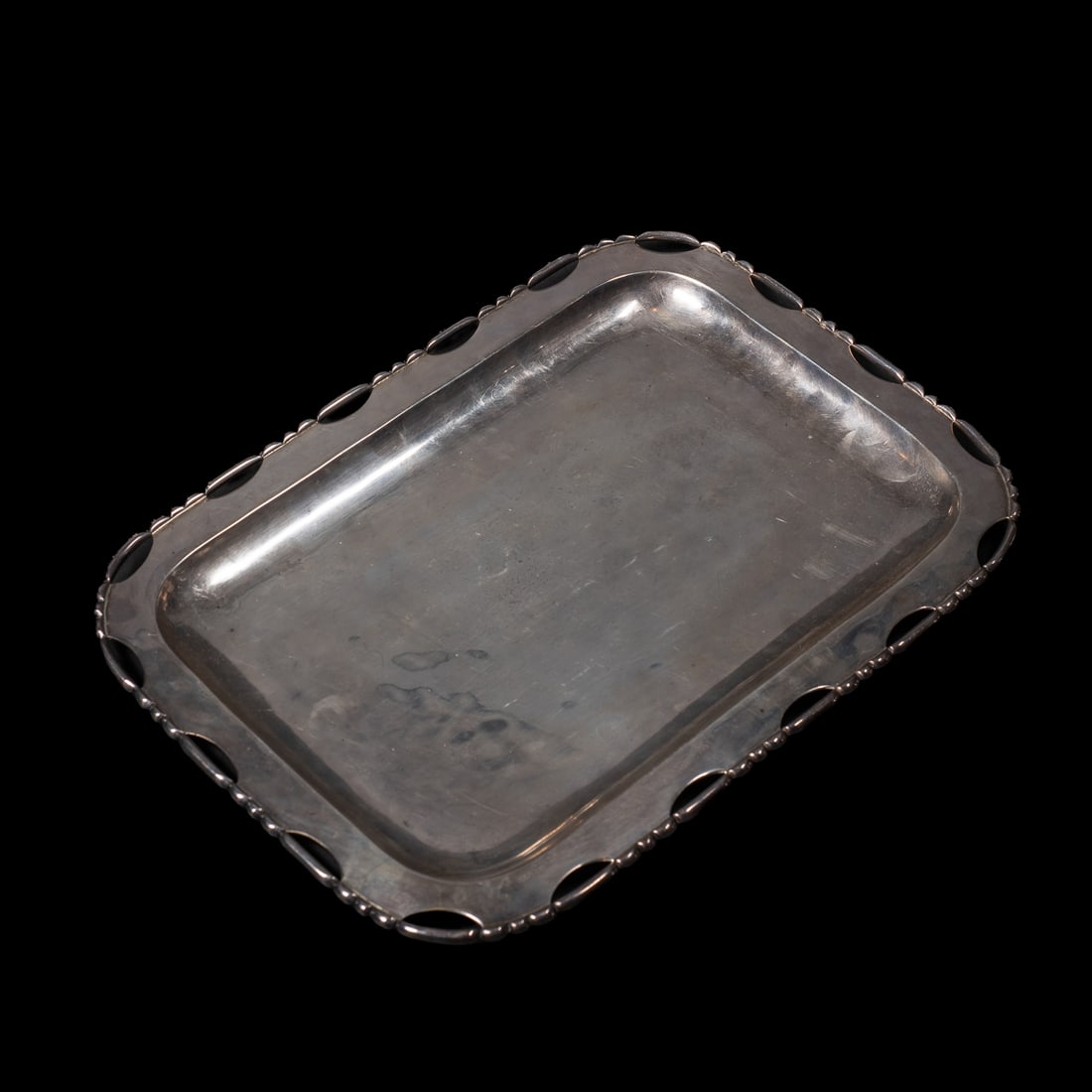 A Hector Aguilar silver tray: The heavy silver rectangular tray with cut out edge and rounded rope rim, marked “Taxco, 940,” with the artists embossed initials. Size 9 ½ x 13 1/8 in. Gross weight 855 grams.
