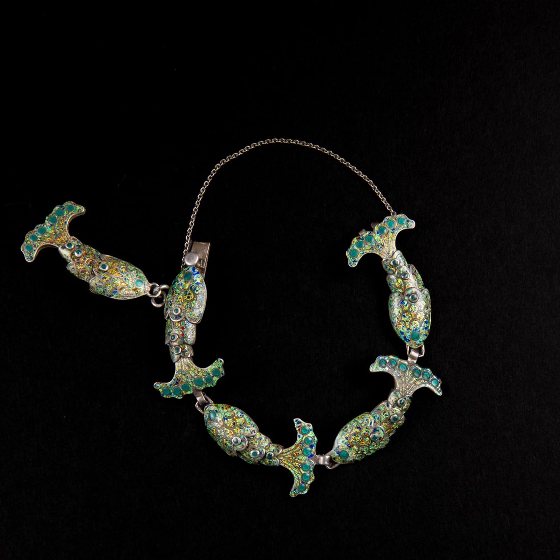 A Margot de Taxco Mexican silver bracelet: Margot Van Voorhies (1896-1985), the Mexican silver bracelet with five articulated fish, decorated with enamel and amethyst settings with silver linked chain attached. Marked “5693. Margot De Taxco