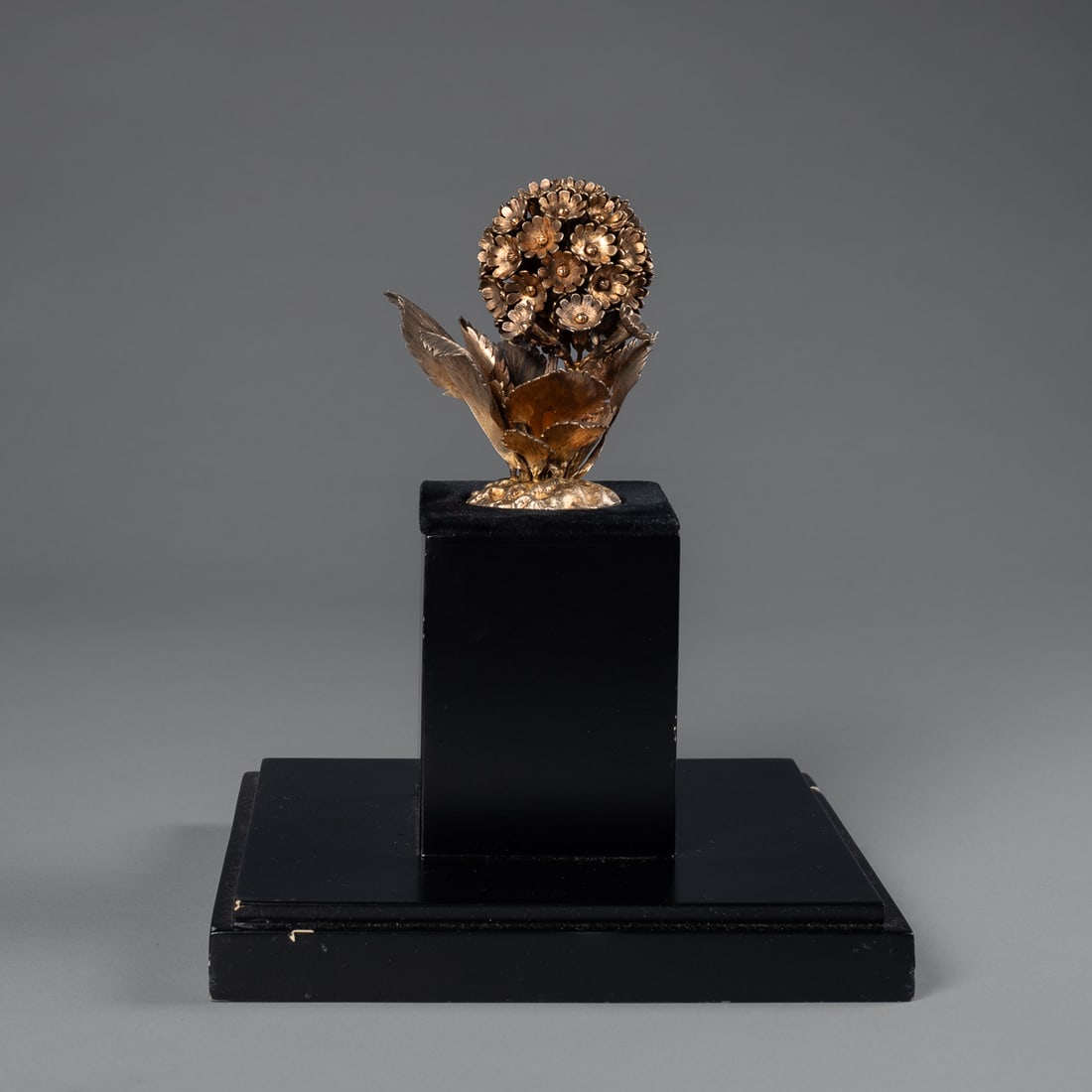 A Janna Thomas De Valarde silver flower group: Standing on a custom wood base, the hydrangea with eight leaves and smaller flower group that combines into ground with roots, marked “Janna Neiman Marcus Sterling Mexico 188.” Overall, gold