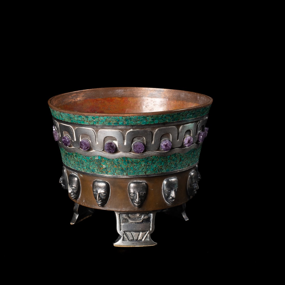 An Enrique Ledesma cache pot: The cache pot with dark and glossy patina, the bowl striped with small turquoise stone mosaic, curved silver detailing, and amethyst circular settings. The bottom ring of protruding cast human faces i