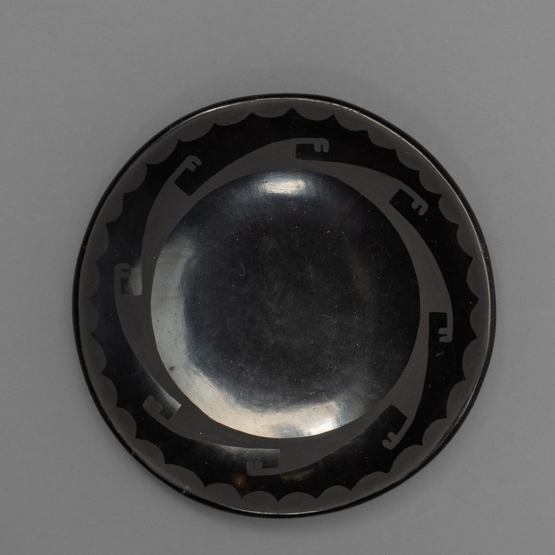 A San Ildefonso blackware plate: Marie + Santana, with wide open center, the design band painted in a negative fashion to depict an abstracted avanyu motif, signed "Marie Santana." Dia. 5 1/2 in.