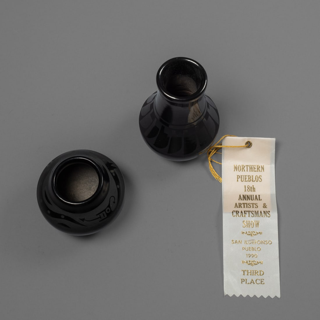 A Margaret Lou Gutierez blackware jar and Denny jar: The miniature vase with negative painted feather pattern below the neck, signed, "Margaret Lou Gutierez," with a smaller jar with avanyu design, signed "Denny." Ht. 5, wd. 3, and ht. 2 3/4, wd. 3 in.