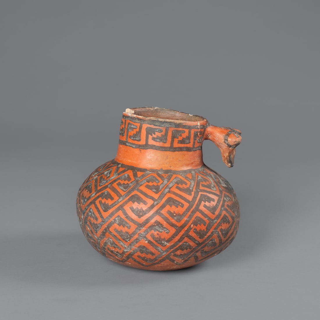 A Pinedale black-on-red pitcher: Circa 1200-1300 A.D., the body decorated with black interlocking key designs on a red ground, with animal head handle, (rim loss and handle re-attached), with inventory number and label on the