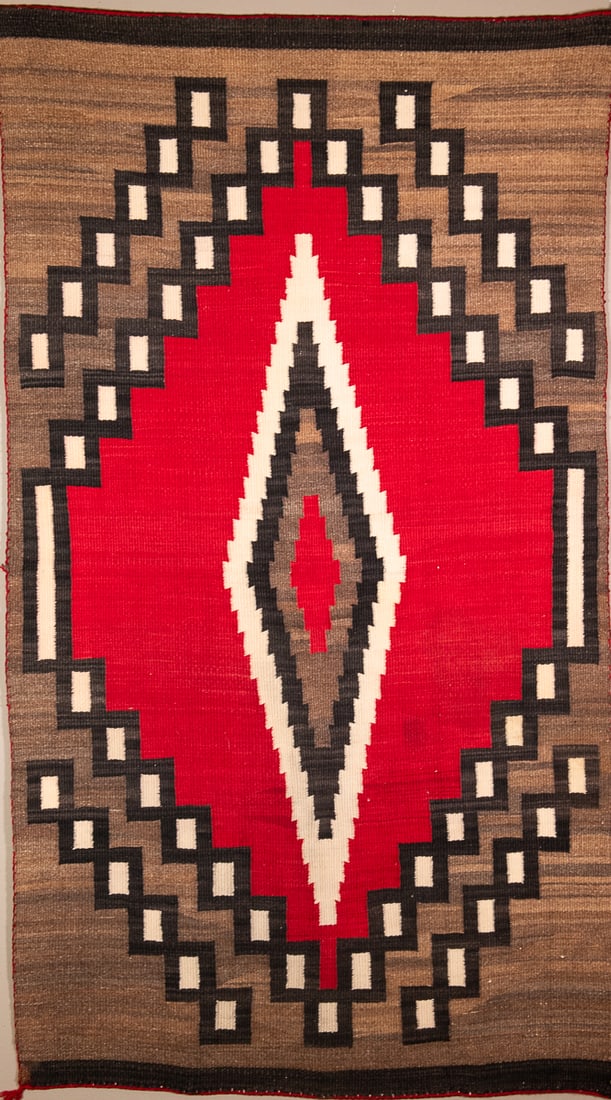A Navajo Ganado rug: Circa 1920s, with a central serrated diamond device on a red background, with surrounded rectangular stepped devices on variegated background. Size 64 1/4 x 36 1/2 in.