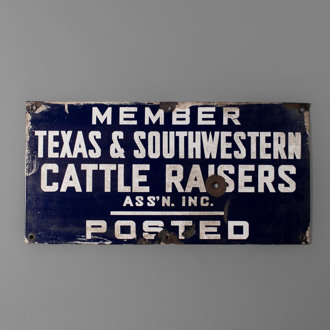A Texas enamel sign: Early 20th century, the metal enameled sign “Member Texas & Southwestern Cattle Raisers Ass’n. Inc. Posted.” Pierced at corners and middle, top, and bottom, with single bullet hole. Size 10 