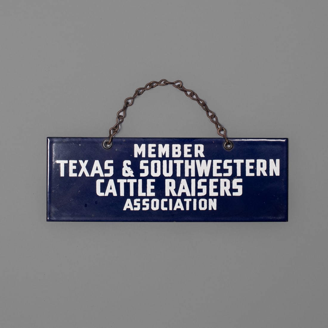 A small Texas enamel sign: “Member Texas & Southwestern Cattle Raisers Association,” with link chain at top. Size 3 ½ x 10 in. Provenance: The Tom Joyce Collection, Santa Fe, NM.