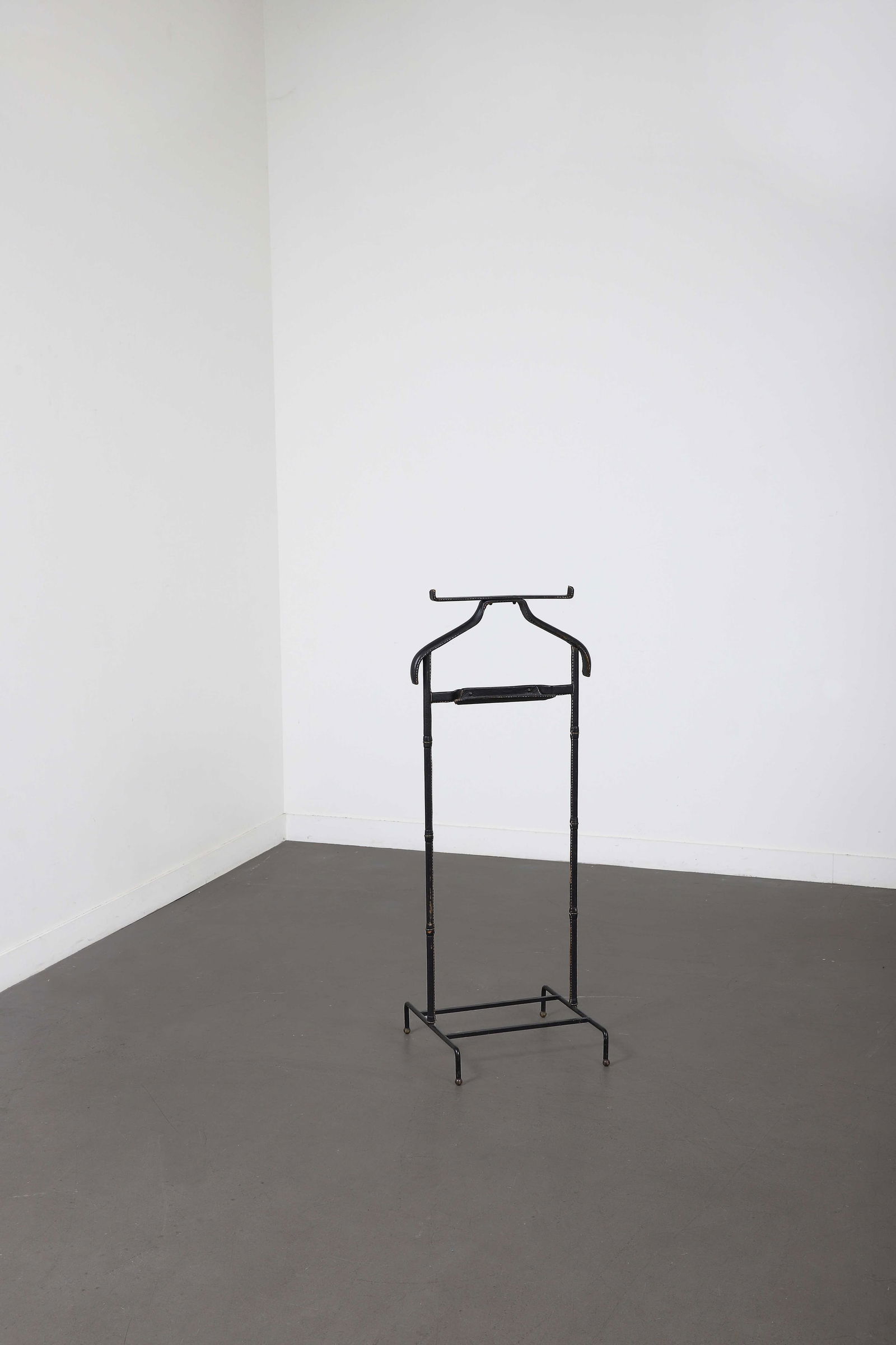 Jacques ADNET (1901-1984): Valet de nuit, circa 1955, à structure en métallaqué noir gainée de cuir piqué sellier noir,reposant sur un piètement en double U àréception boules en laiton.(U