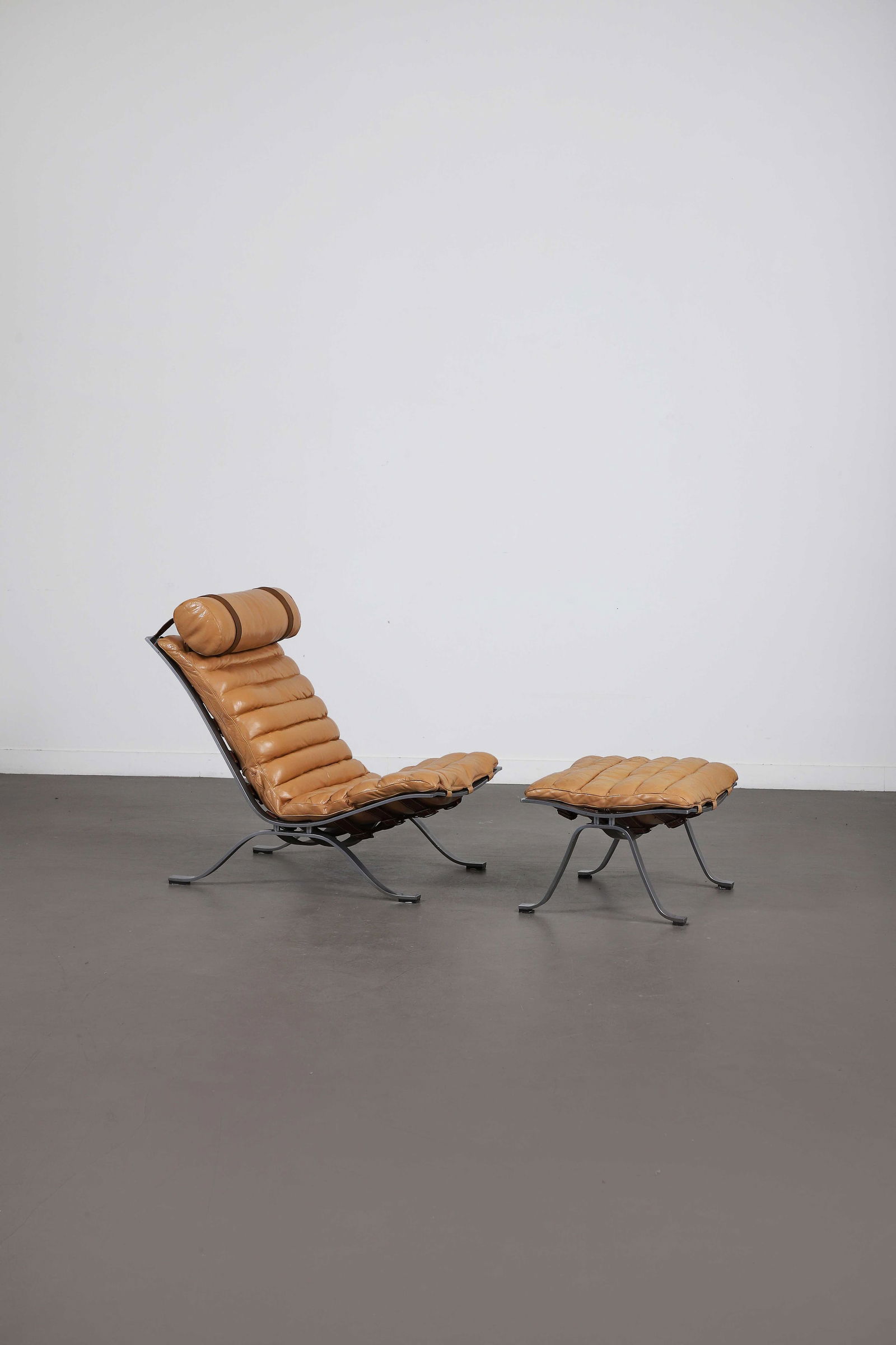 Arne NORELL (1917-1971): Fauteuil et son repose pied modèle Ari, 1966,à coussins d’assises en cuir marron disposéssur une structure en lames d’acier formant unpiètement quadripode.(Griffures, u