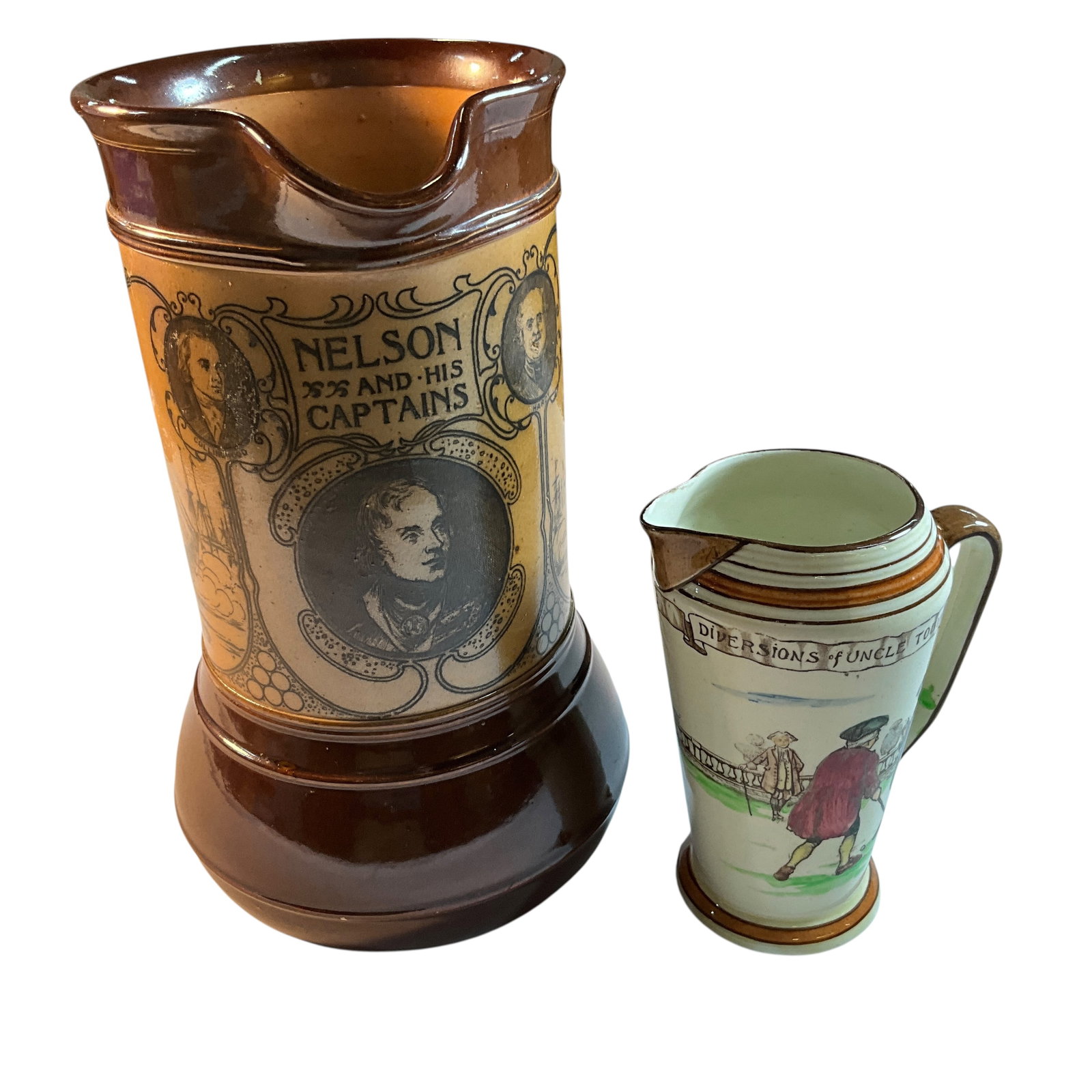 Two Royal Doulton Pitchers: Two Royal Doulton Pitchers- A Trafalgar Commemorative pitcher of "Nelson and His Captains," with portraits and battle scenes on the side panels. The handle was broken off at some point, and has an old