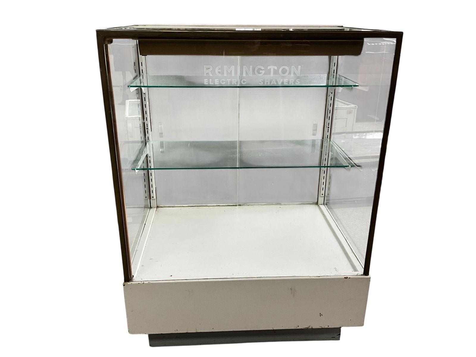 Vintage Remington Shavers Display Case: Glass Display case, with two glass shelves and a rear drawer. Frosted glass doors and the words "Remington Electric Shavers" etched in the front glass panel. There is an electric plug and light