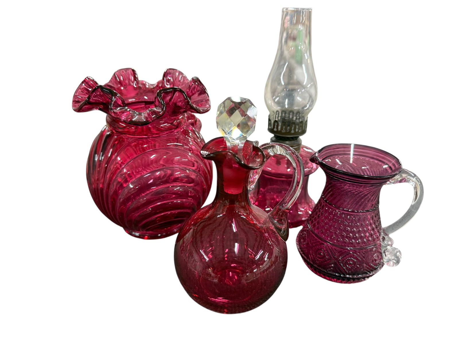 Cranberry Glass Lot: Cranberry Glass Lot. A Fenton Caprice with Bow and Drape Vase, approx. 6.5" high, a Pilgrim Glass Bennington pitcher, a blown glass cruet with faceted stopper, and a miniature oil lamp with cranberry