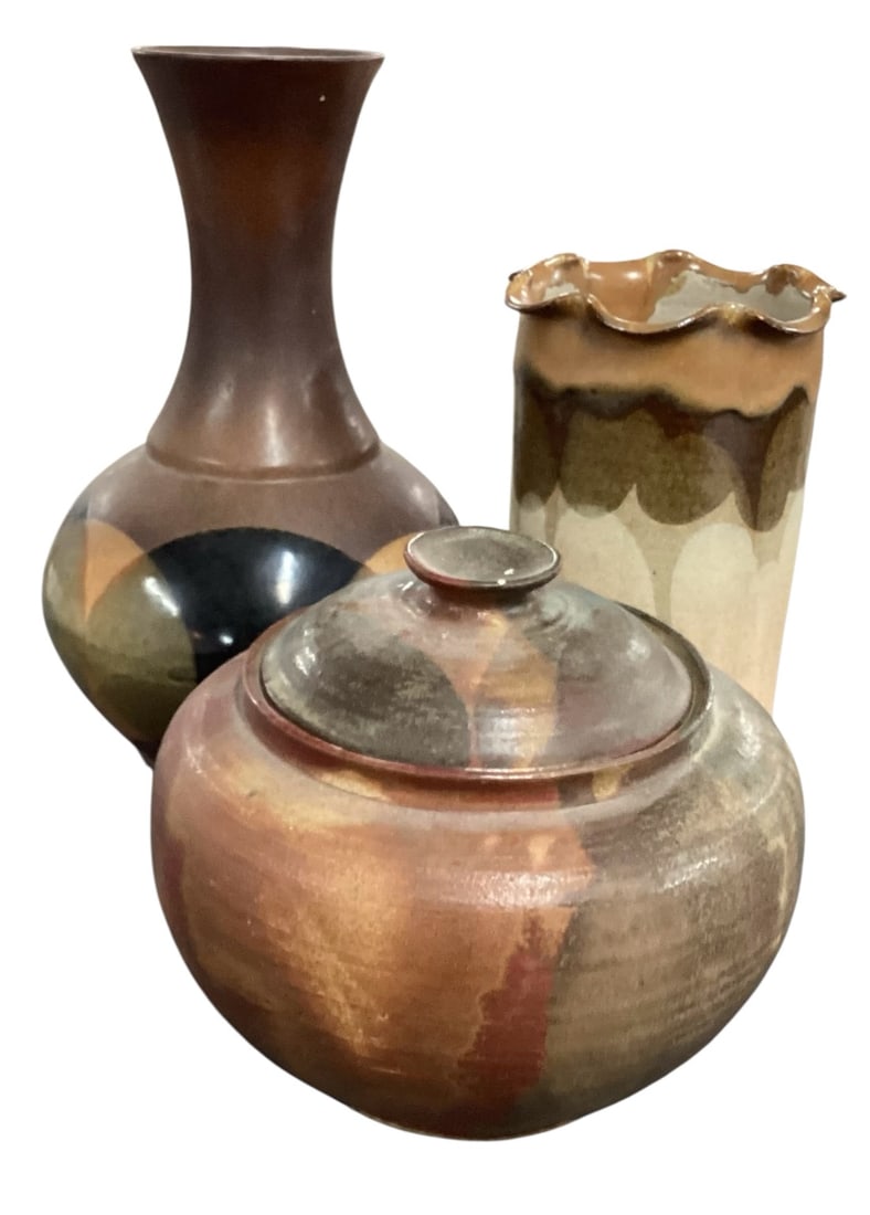 Three Studio Pottery Vessels Including Lidded Jar, Vase, and Signed 1999 Piece: A group of three studio pottery vessels featuring varied forms and earthy glaze treatments. Includes a rounded lidded jar with fitted lid, finished in warm brown and rust-toned glazes with subtle vert