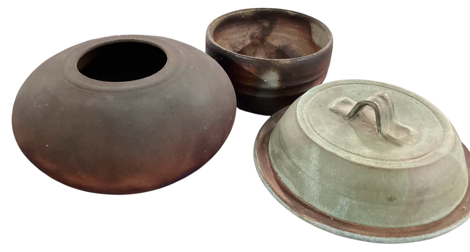 Three-Piece Studio Pottery Group Including Covered Dish, Low Vase, and Bowl: A three-piece grouping of studio pottery showcasing organic forms and earthy, reduction-fired finishes. Includes a low, wide-mouthed vessel with a flattened, rounded body and narrow opening, finished 