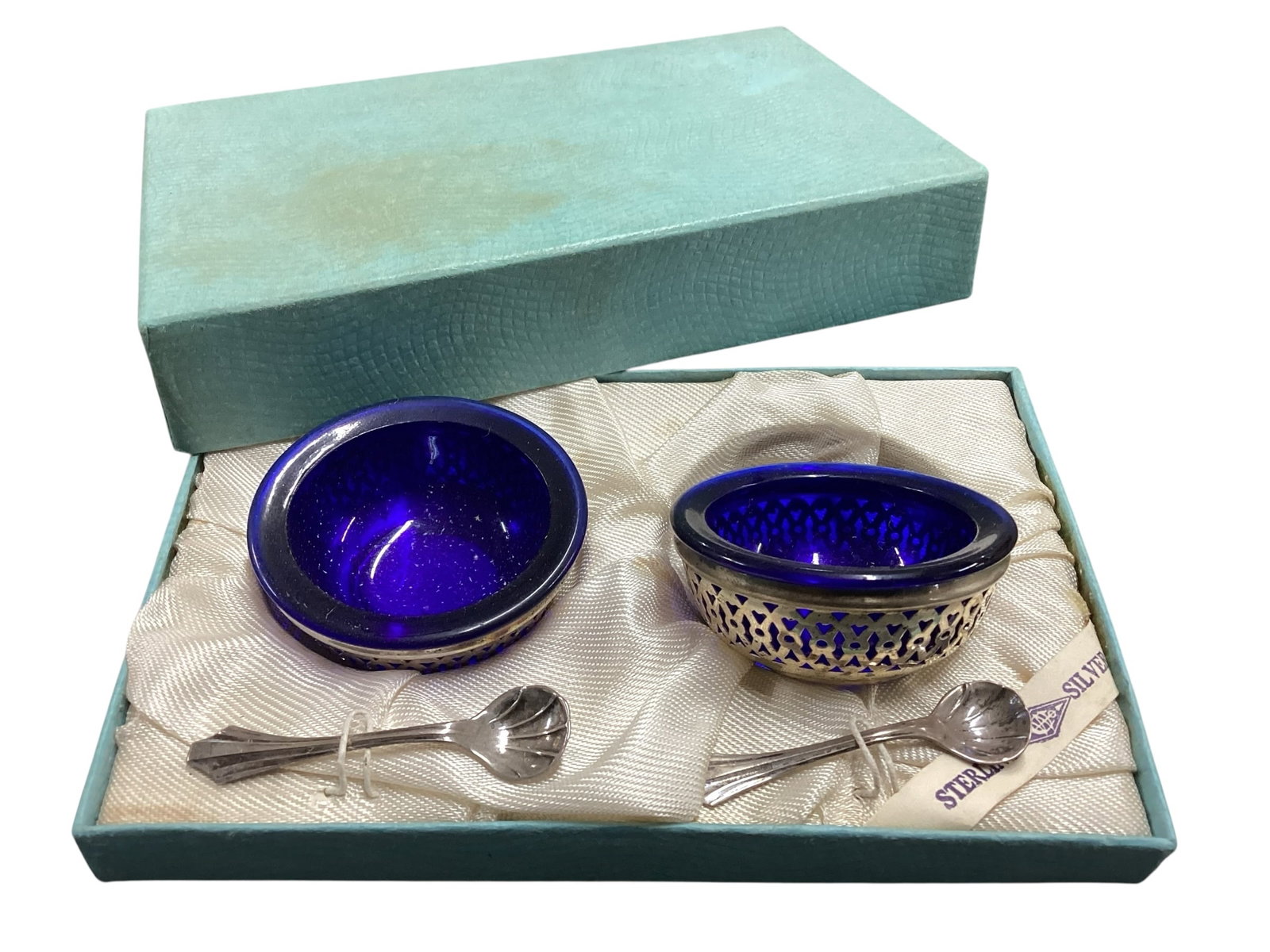 Pair of Sterling Silver and Cobalt Glass Salt Cellars with Spoons in Original Box: Pair of sterling silver and cobalt glass salt cellars with matching spoons in original box. Set includes two pierced silver holders with cobalt blue glass liners and two small sterling spoons. Box con