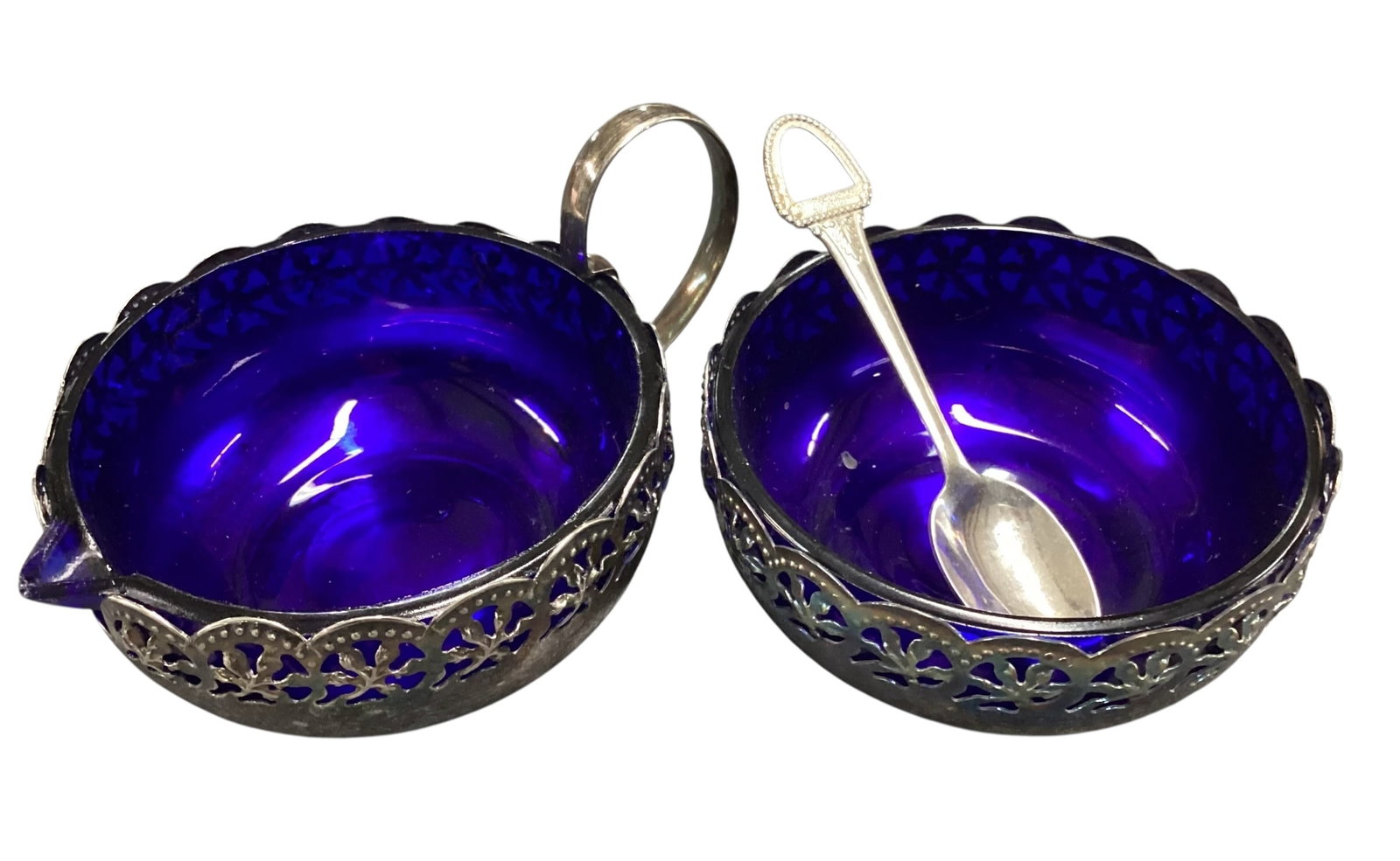 Silver Plate Creamer and Open Sugar Bowl with Cobalt Blue Glass Liners and Spoon: Vintage silver plate cream and sugar set featuring cobalt blue glass liners within pierced floral-pattern silver plate holders. The set includes a handled creamer with pouring spout and a matching ope
