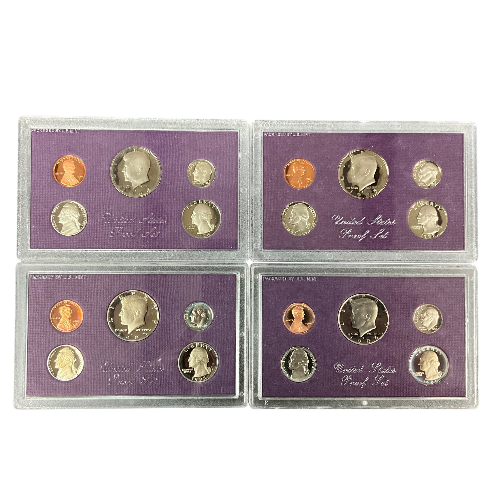 Group of United States Proof Sets, 1984-1986: Group of United States Proof Sets housed in original purple Mint packaging, including one 1984 set, two 1985 sets, and one 1986 set. Sets include the standard proof coin denominations in hard plastic 