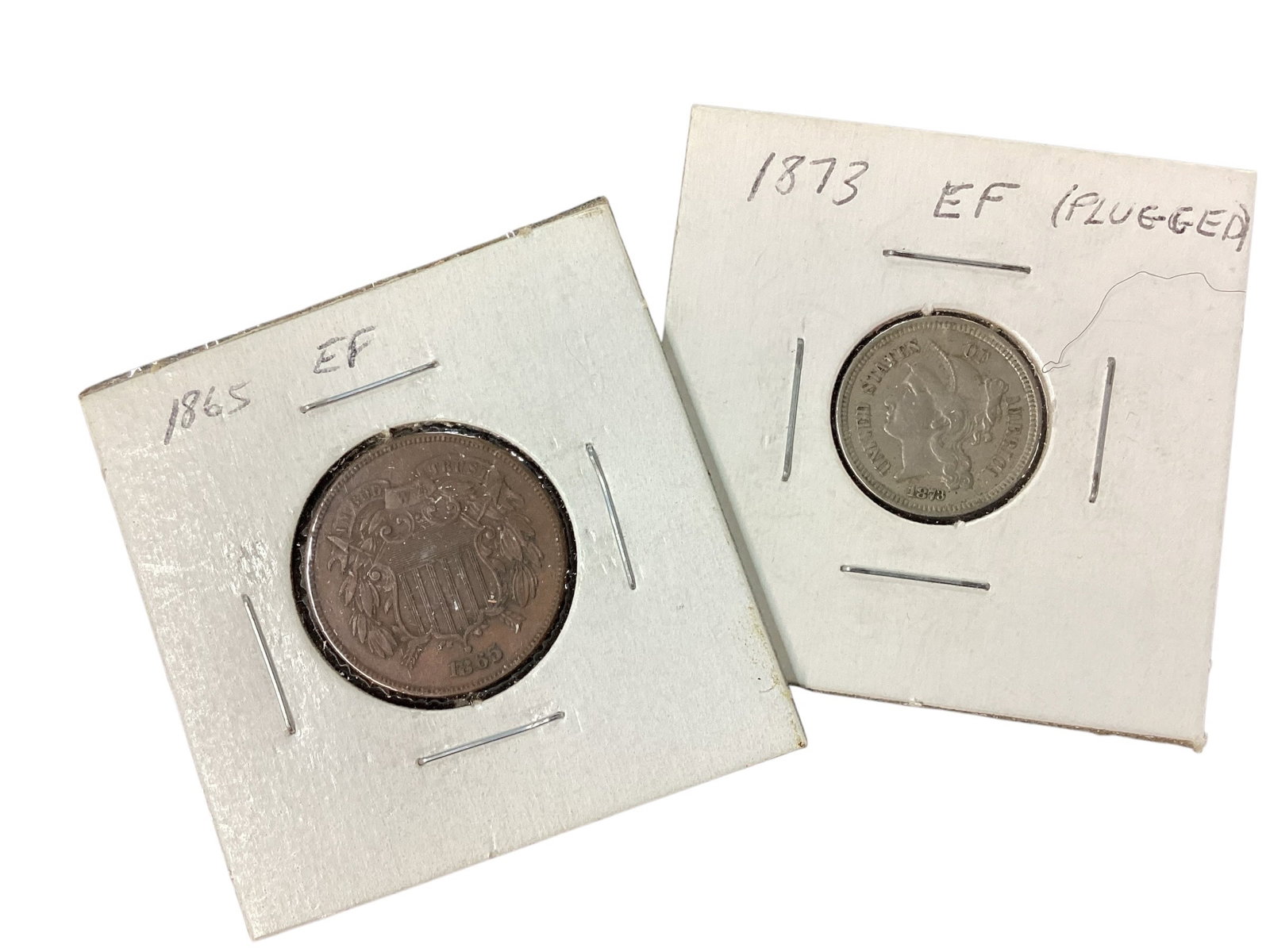 1865 Two-Cent Piece and 1873 Three-Cent Nickel Coins: Two-piece United States coin collection featuring an 1865 Two-Cent Piece and an 1873 Three-Cent Nickel. The 1865 coin displays the shield obverse with large “2 CENTS” reverse wreath design and