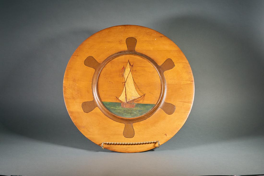 Wooden Wall Ship Plaque: Wooden wall plaque with inlay of a ships wheel. 20" diameter. Painting of sail boat in center.