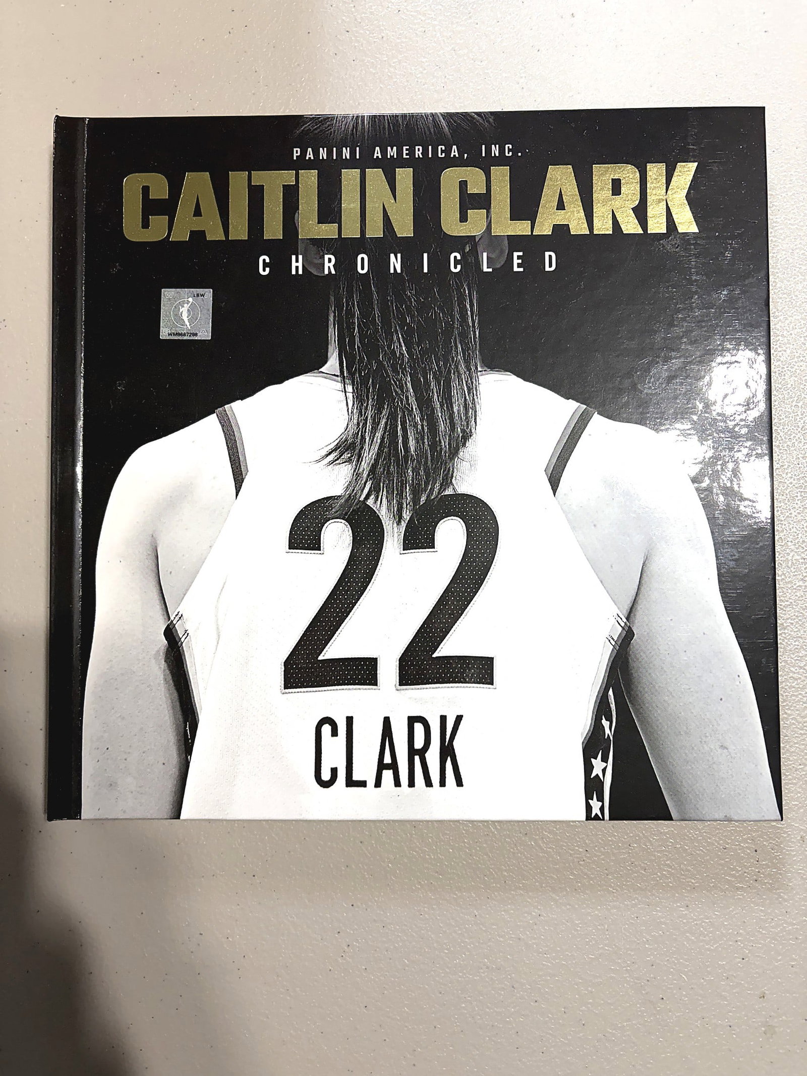 2025 Panini Chronicled Caitlin Clark Basketball: This is the Caitlin Clark Chronicled hardcover book published by Panini America, Inc. The cover features a black-and-white close-up of Caitlin Clark's jersey back displaying her iconic number 22 and