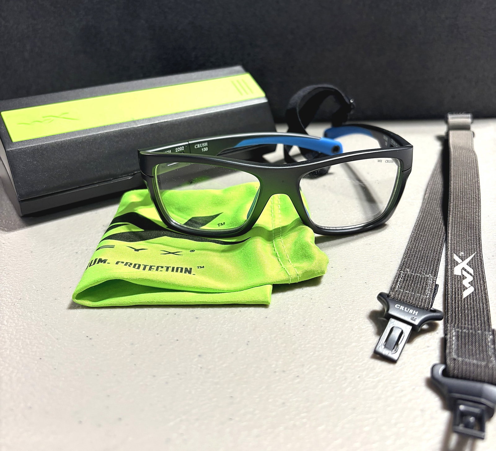 Wiley X WX Crush 2110 Gray/Blue Sunglasses: This listing features a Wiley X WX Crush safety eyewear set, model number 2202, frame size 130. The frame is black with blue accent temples and fitted with clear lenses. The set includes the original