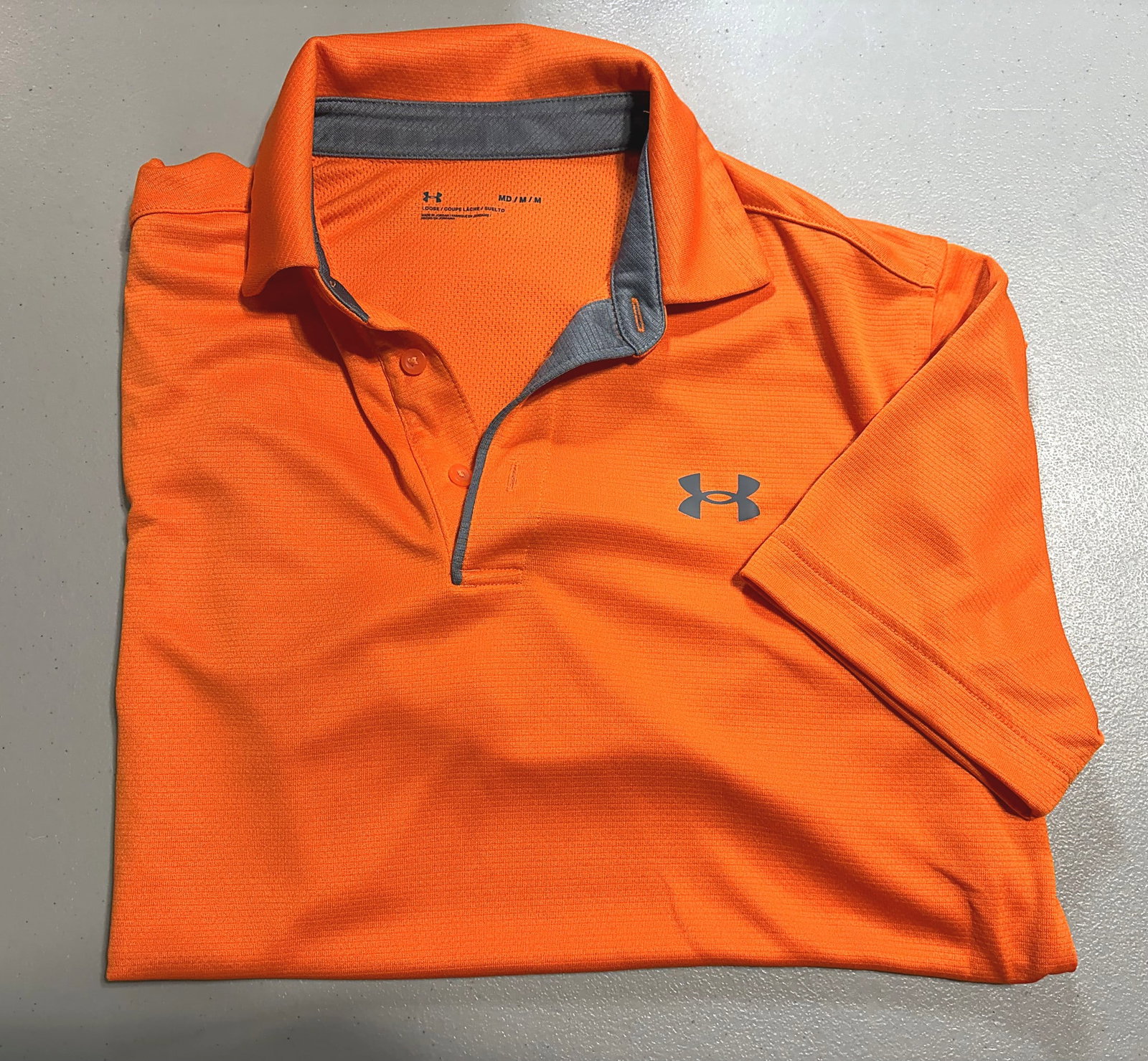 Under Armour Men's Orange Performance Polo Shirt: This is an Under Armour men's polo shirt in a bright orange colorway with gray accent details on the collar interior and placket. The shirt features Under Armour's signature moisture-wicking