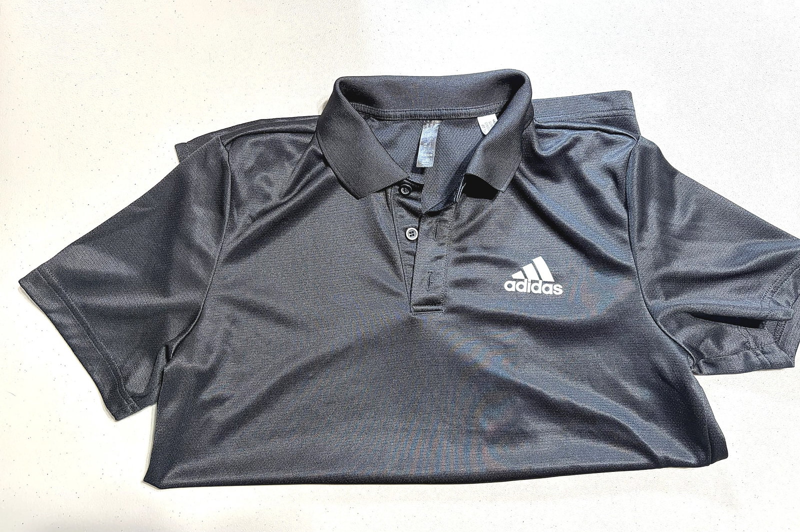 Adidas Men's Dark Gray Heather Performance Polo: This is a dark charcoal gray heather performance polo shirt by Adidas, featuring the iconic three-stripe Adidas logo embroidered on the left chest. The shirt is a short-sleeve polo style with a
