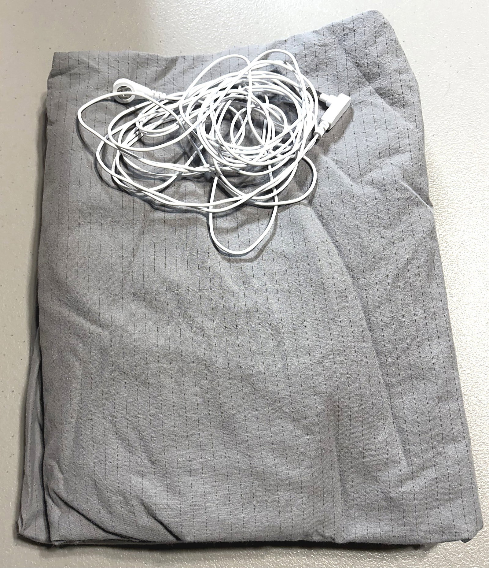 Grounding Earthing Sheet w/ Cord Gray Striped: This listing features a folded gray fabric sheet with a fine conductive stripe pattern throughout the textile, accompanied by a long white grounding cord with snap connectors and a standard outlet