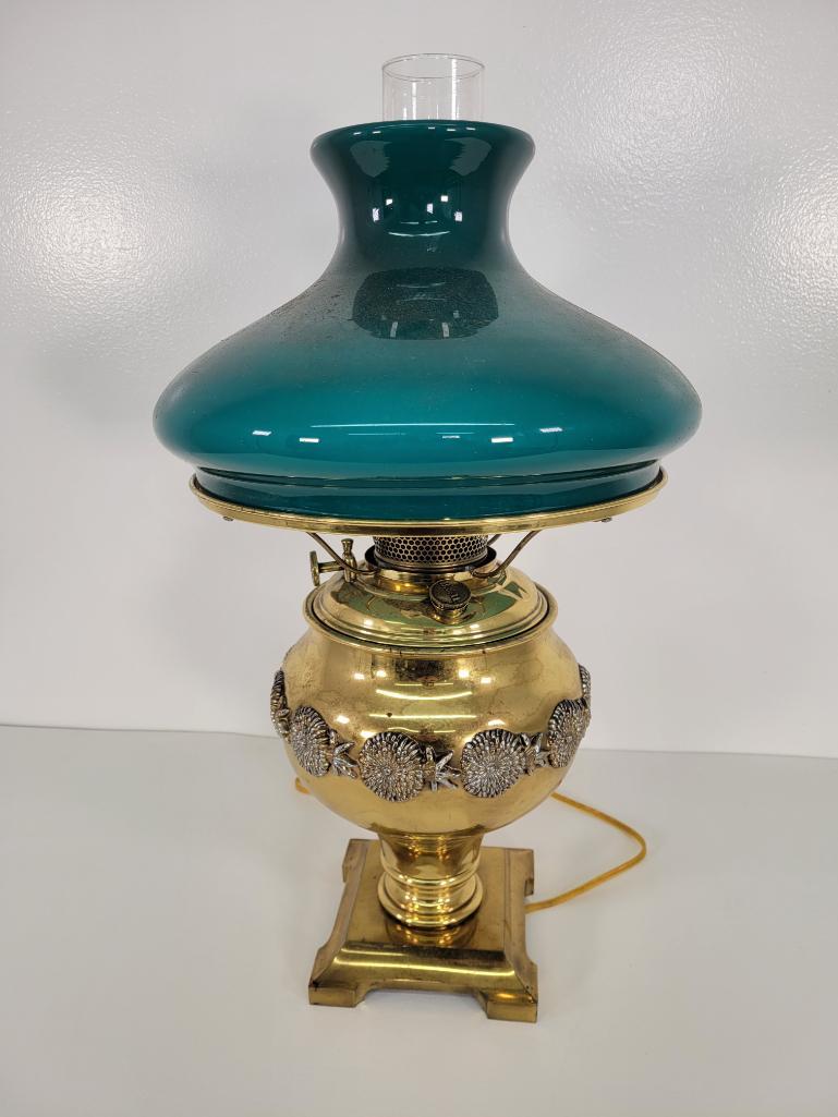 Bradley & Hubbard Brass Banquet Lamp: Description: This lot include an antique banquet lamp made by Bradley & Hubbard. The lamp base is made of polished brass with a floral design going around it. Includes a Green glass shade and chim