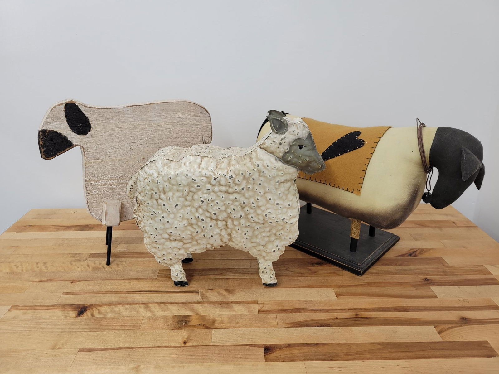 Lot of 3 Folk Art Sheep Statues: The lot includes the 3 unique folk art style sheep figures, One is made of cloth, one of metal, and one of wood. Each appears vintage in age, 20th century.Measurements: Largest piece is 18.5"L x 7"W x