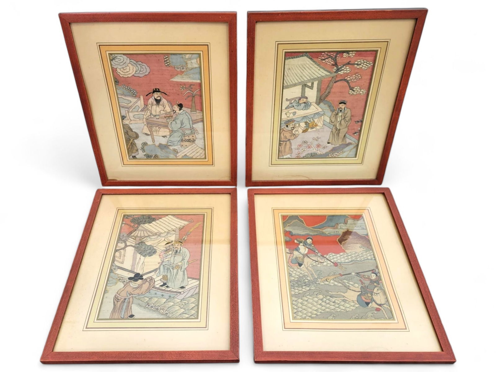 Set of Four Japanese Paintings on Fabric: A set of four framed Japanese paintings on fabric, each depicting scenes from traditional Japanese life. The paintings are housed in matching red wooden frames and show signs of aging, with some fadin