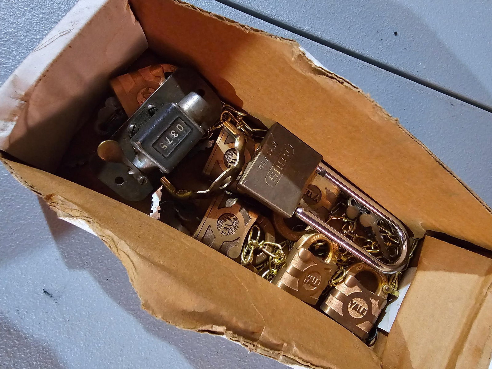 Box of Vintage Padlocks: Box of vintage padlocks, some with attached chains. Includes various sizes and brands. Estate-found condition with some rust and wear. Please see photos for more details Cost to transport this lot bac
